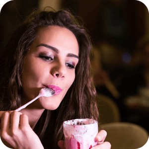 Woman with spoon in her mouth looks at cup of yogurt in her hand