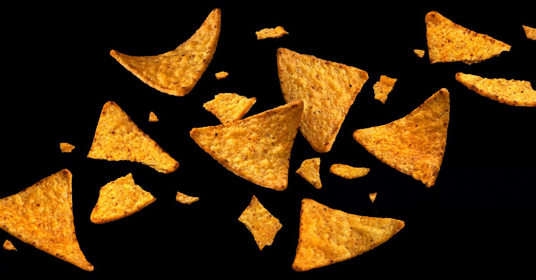 Triangle chips with red seasoning float down on black background